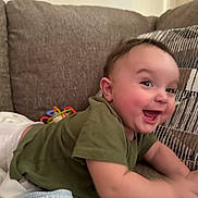 Nolan is registered to the contest to win money with this photo: baby, child, smiling, happy, couch, green_shirt, white_pants, toy, indoor, face, cheeks, eyes, person, infant, cozy, furniture, playful, cute, toddler, home