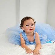 Madison is registered to the contest to win money with this photo: child, toddler, blue_dress, curly_hair, smiling, lying_down, white_background, soft_texture, portrait, cute, innocence, baby, fashion, indoor, happy, person, skin, face, hands, young