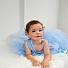 child, toddler, blue_dress, curly_hair, smiling, lying_down, white_background, soft_texture, portrait, cute, innocence, baby, fashion, indoor, happy, person, skin, face, hands, young