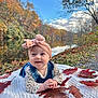 Poppy is registered to the contest to win money with this photo: baby, head_wrap, denim, blanket, autumn_leaves, river, fall_foliage, outdoor, nature, smiling, child, grass, sky, clouds, tree, water, seasonal, cute, portrait, happy
