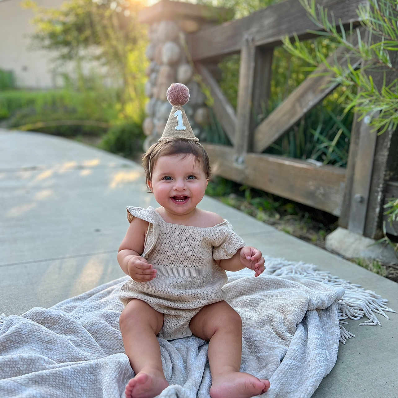 Ellia is registered to the contest to win money with this photo: baby, blanket, bodypart, clothing, dress, face, finger, grass, hand, happy, head, outdoors, person, photography, plant, portrait, sitting, smile, summer, wood