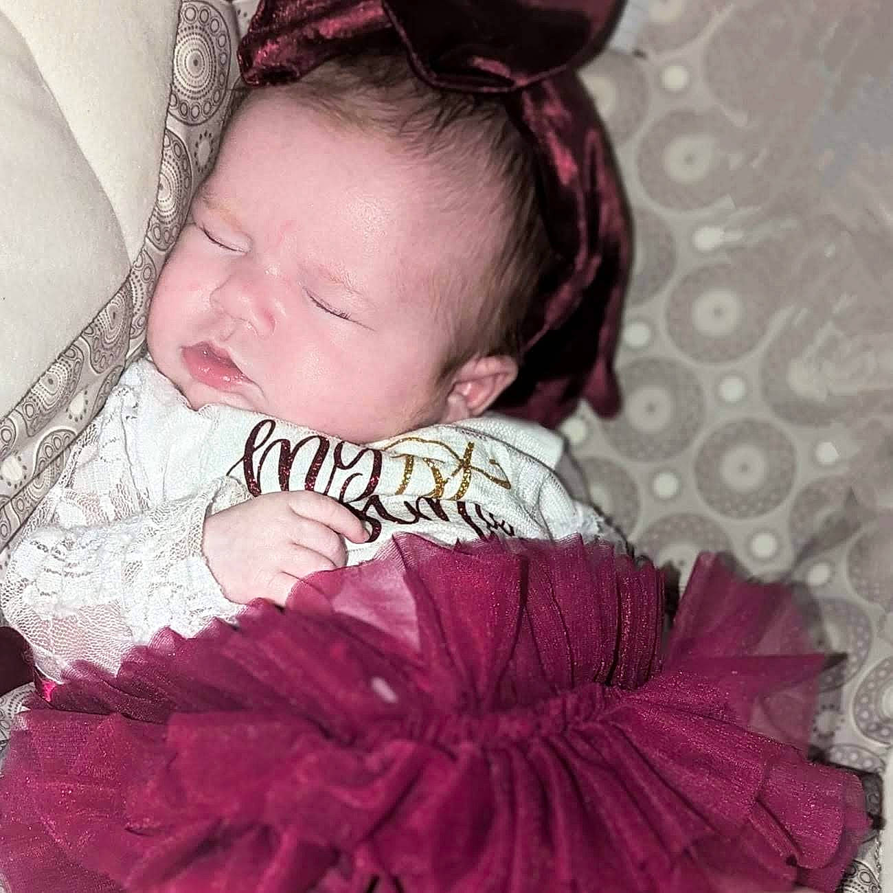 Joelene is registered to the contest to win money with this photo: baby, baby_sleeping, baby_toddler_clothing, black_hair, comfort, couch, eyelash, hairstyle, happy, headgear, headpiece, iris, linens, magenta, neck, pattern, person, petal, pink, sleeve