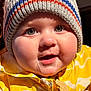 child, baby, infant, beanie, knit_hat, jacket, yellow, drool, cheeks, close_up, portrait, smiling, eyes, rosy_cheeks, winter_clothing, zipper, hands, candid, indoor, warm_lighting