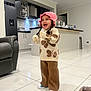 toddler, child, indoor, kitchen, smiling, laughing, hat, pink, sweater, butterfly, pants, brown, white_shoes, tile_floor, furniture, refrigerator, cabinet, counter, blanket, happy