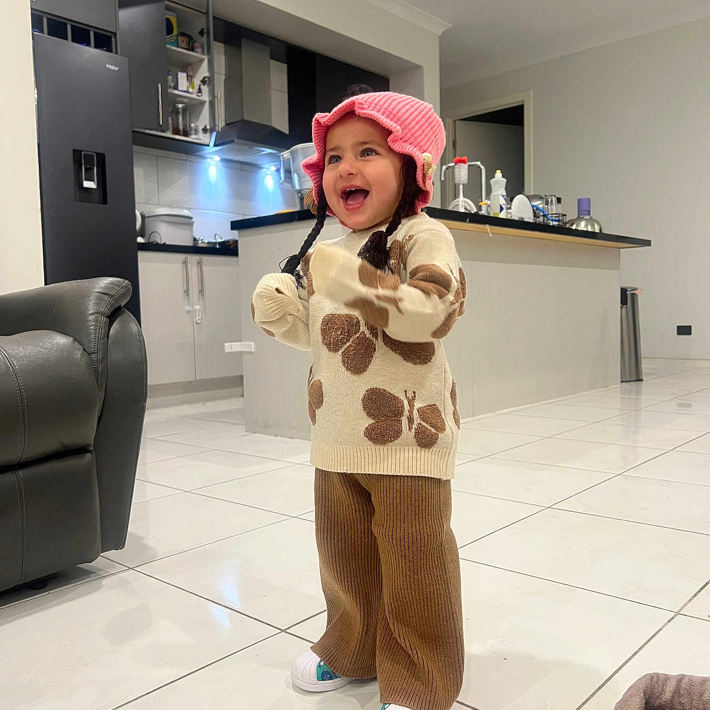 Anubhavi Kaur is registered to the contest to win money with this photo: blanket, brown, butterfly, cabinet, child, counter, furniture, happy, hat, indoor, kitchen, laughing, pants, pink, refrigerator, smiling, sweater, tile_floor, toddler, white_shoes