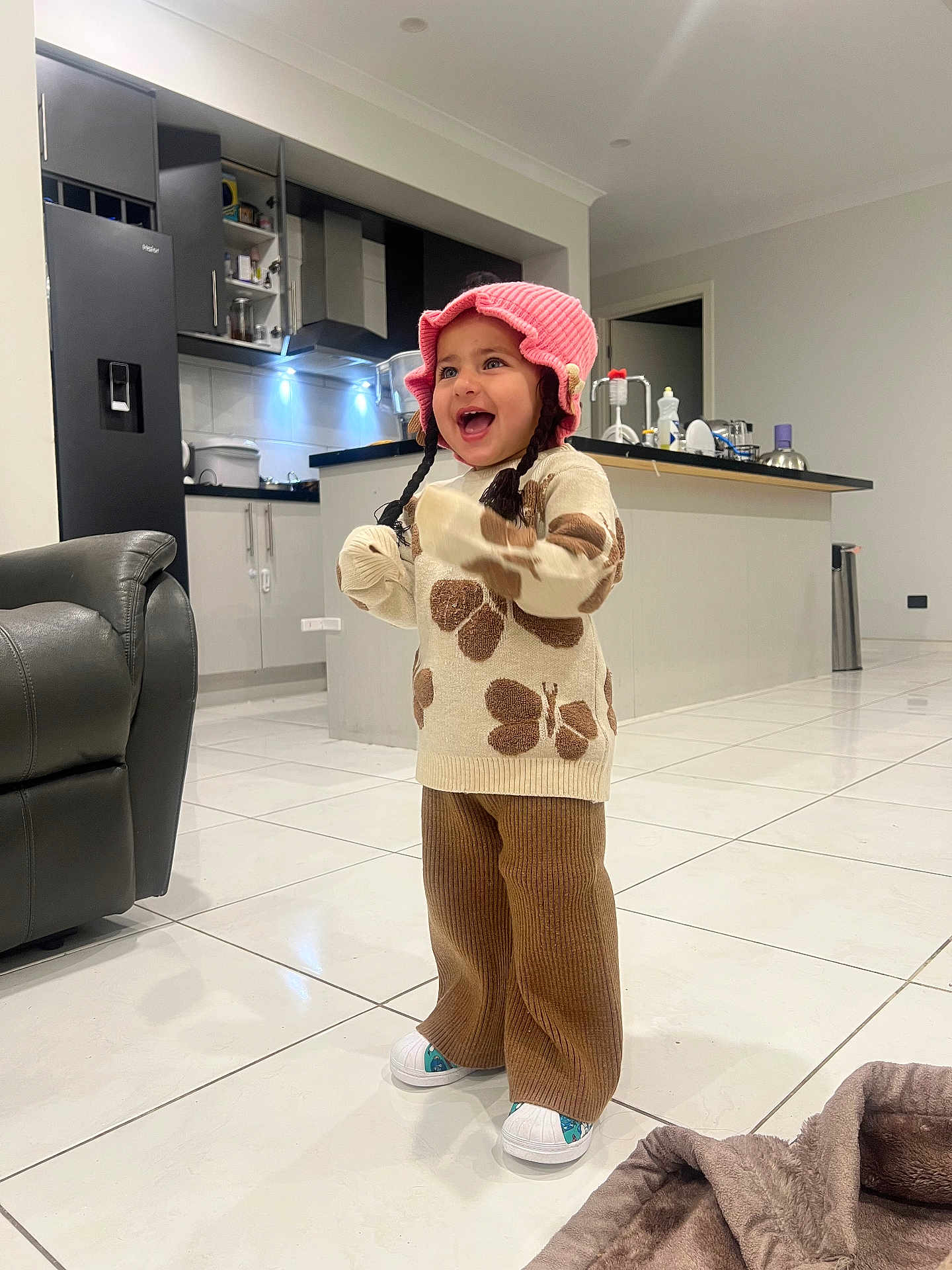 Anubhavi Kaur is registered to the contest to win money with this photo: toddler, child, indoor, kitchen, smiling, laughing, hat, pink, sweater, butterfly, pants, brown, white_shoes, tile_floor, furniture, refrigerator, cabinet, counter, blanket, happy