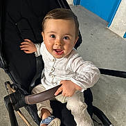 Andrea a rejoint le concours — aidez-le/la à gagner de superbes lots ! baby, blue_door, child, clothing, concrete_floor, face, footwear, grip, hand, happy, indoor, pants, person, portrait, sandals, seated, smile, stroller, toddler, white_shirt