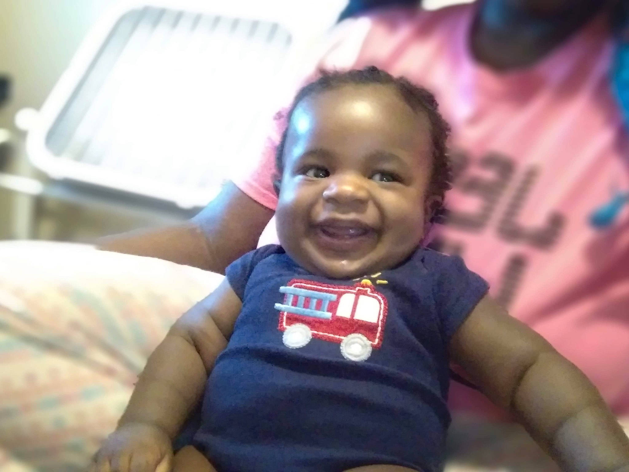 Mario is registered to the contest to win money with this photo: arm, baby, baby_toddler_clothing, cheek, child, event, fun, gesture, happy, iris, joy, laugh, mouth, nose, person, sitting, skin, smile, t_shirt, thumb