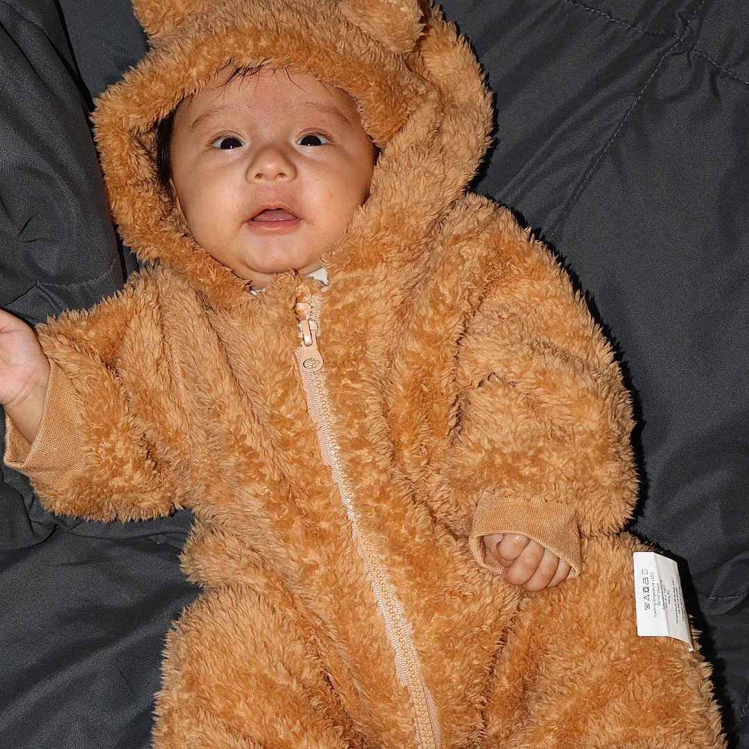Prashil Khanal joined the competition — help win amazing prizes! baby, infant, child, costume, bear_suit, fluffy, cute, portrait, indoor, clothing, face, expression, hand, foot, sleepwear, soft, warm, quilted_background, zipped, hood