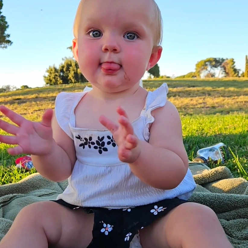 Krysleine is registered to the contest to win money with this photo: baby, blanket, child, clothing, cute, daylight, grass, hands, happy, nature, outdoor, park, person, playful, sitting, summer, sunlight, tongue, trees, young