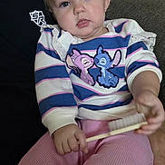 Krysleine is registered to the contest to win money with this photo: toddler, child, baby, pink_bow, striped_shirt, cartoon_characters, brush, couch, indoor, person, cute, portrait, sitting, hand, clothing, face, hair, expression, comfort, home