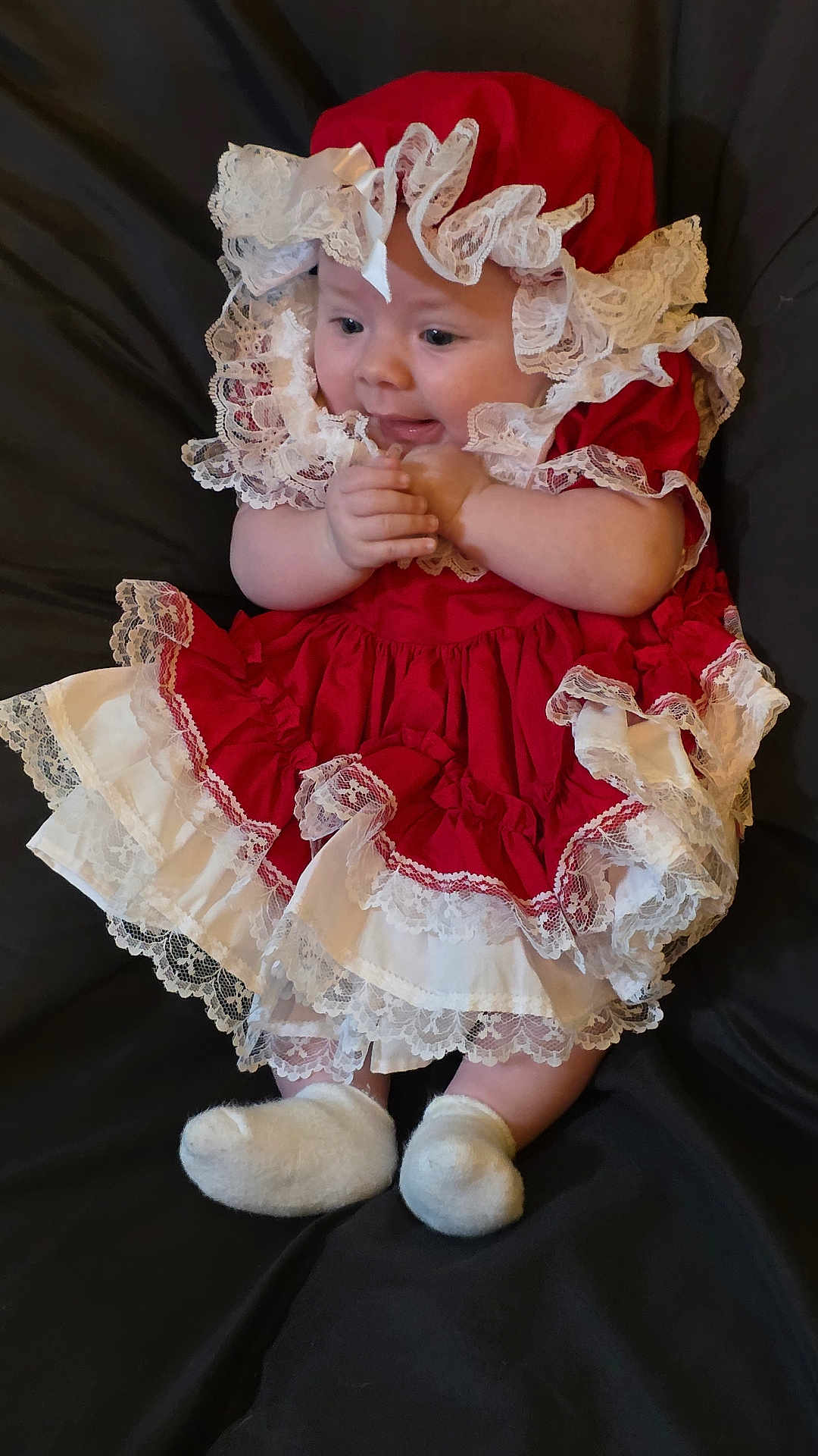 Kelly Kay Sheets joined the competition — help win amazing prizes! baby, infant, child, red_dress, lace, frills, bonnet, white_socks, cute, portrait, sitting, fabric_background, soft_lighting, hands, smiling, face, eyes, indoor, clothing, young