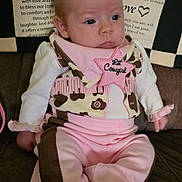 Kelly joined the competition — help win amazing prizes! baby, infant, child, pink_clothing, brown_clothing, cowgirl_outfit, star_patch, sitting, couch, quilt, patchwork, text, face, hands, feet, sock, indoor, portrait, cute, curious