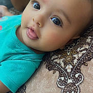 Athena is registered to the contest to win money with this photo: baby, child, face, tongue, blue_shirt, patterned_blanket, close_up, cute, infant, portrait, lying_down, skin, eyelashes, expression, soft_light, indoors, person, head, young, curious