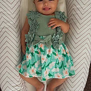 Athena is registered to the contest to win money with this photo: baby, infant, child, smiling, dress, headband, bow, floral, pattern, cushion, lounger, chevron_pattern, fabric, feet, hand, person, cute, happy, indoors, lying_down