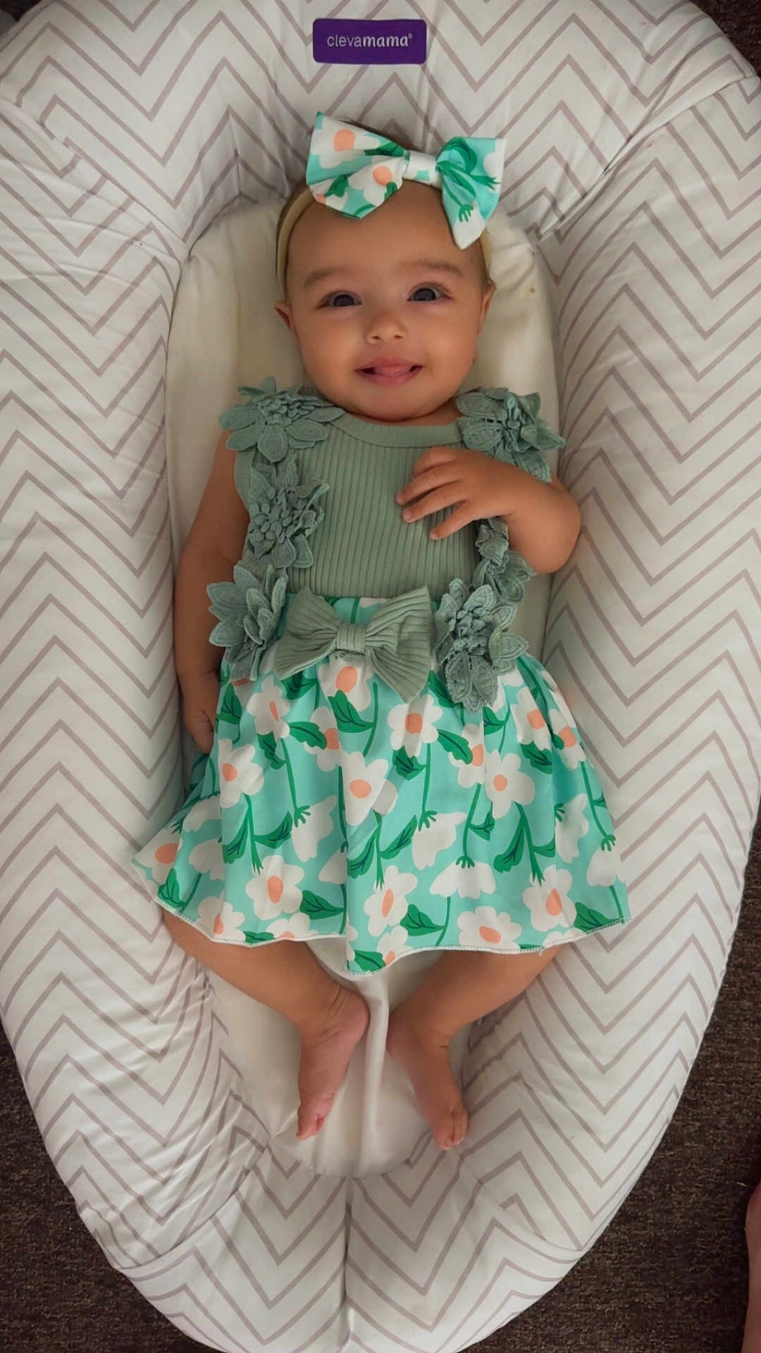 Athena is registered to the contest to win money with this photo: baby, infant, child, smiling, dress, headband, bow, floral, pattern, cushion, lounger, chevron_pattern, fabric, feet, hand, person, cute, happy, indoors, lying_down