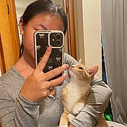Juno is registered to the contest to win money with this photo: person, cat, indoor, selfie, phone, mirror, gray_clothing, orange_cat, white_cat, holding, looking_up, door, curtain, earrings, ring, long_hair, reflection, furniture, casual, home