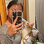 person, cat, indoor, selfie, phone, mirror, gray_clothing, orange_cat, white_cat, holding, looking_up, door, curtain, earrings, ring, long_hair, reflection, furniture, casual, home