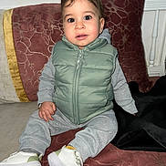 Ziyad a rejoint le concours — aidez-le/la à gagner de superbes lots ! toddler, child, sitting, indoor, clothing, vest, sneakers, couch, pillow, face, person, cute, young_child, casual_wear, footwear, expression, portrait, home, cozy, curious