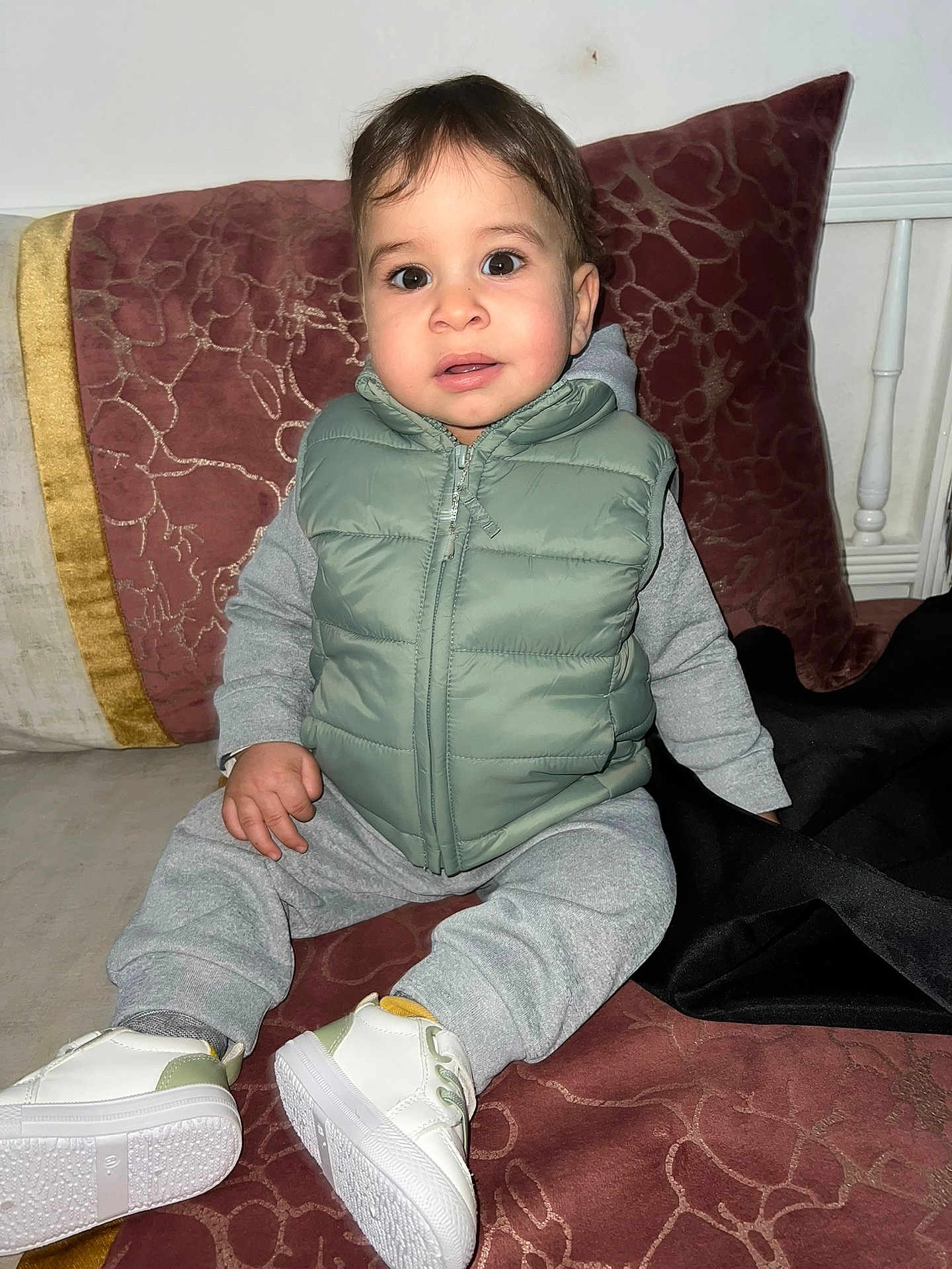 Ziyad a rejoint le concours — aidez-le/la à gagner de superbes lots ! toddler, child, sitting, indoor, clothing, vest, sneakers, couch, pillow, face, person, cute, young_child, casual_wear, footwear, expression, portrait, home, cozy, curious