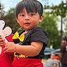 Mateo is registered to the contest to win money with this photo: birthday, black_shirt, bow_tie, celebration, child, crown, mickey_mouse, outdoor, party, people, playground, portrait, red_clothing, smiling, social_media_screenshot, standing, stuffed_animal, toddler, toy, trees
