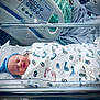 newborn, baby, hospital, bassinet, blanket, blue_hat, swaddled, sleeping, medical_equipment, bed, infant, footprints, person, healthcare, patient, cute, peaceful, indoors, resting, nursery