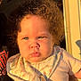 Jalaya is registered to the contest to win money with this photo: baby, child, curly_hair, bib, sunlight, portrait, face, expression, indoors, doorway, clothing, person, cute, infant, holding, skin, cheeks, young, serious, light