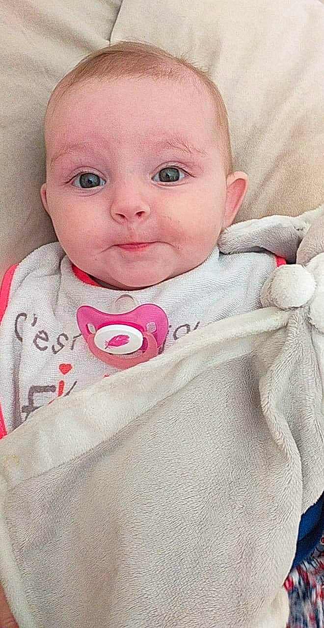 Maëlyne participe au concours pour gagner de l'argent avec cette photo : baby, baby_products, baby_toddler_clothing, blanket, cheek, child, eye, face, head, linens, lip, nose, person, pink, product, skin, smile, textile, toddler