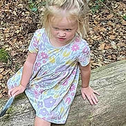 Amelia-Mae is registered to the contest to win money with this photo: child, girl, forest, log, leaves, nature, outdoor, dress, floral_pattern, sneakers, feather, tree, woodland, playful, casual_clothing, top_knot, sitting, young_child, daylight, curly_hair