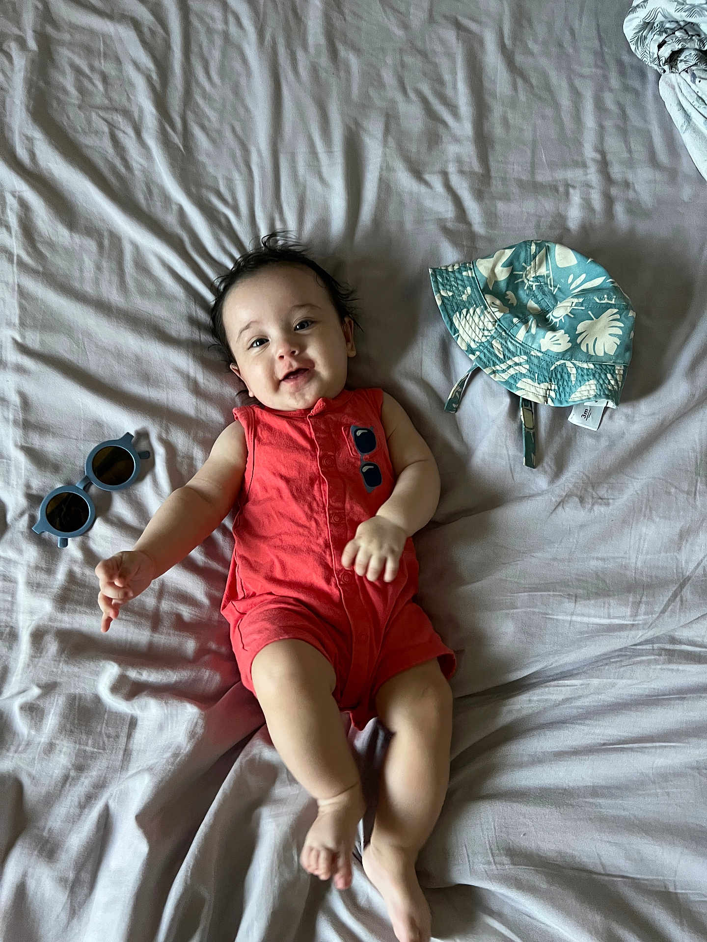 Peter joined the competition — help win amazing prizes! baby, infant, smiling, lying_down, bed, bedding, romper, clothing, hat, sunglasses, happy, cute, skin, person, indoor, child, young, relaxed, accessory, fashion