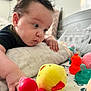 Peter is registered to the contest to win money with this photo: baby, child, toy, rubber_duck, bed, pillow, hand, face, curly_hair, indoor, focus, colorful, play, childhood, person, soft, expression, cute, close_up, infant