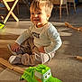 child, toddler, toy, green_toy, truck, smiling, indoor, floor, wooden_table, chair, wicker_chair, sunlight, happy, play, person, clothing, home, furniture, room, kids