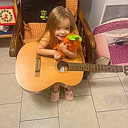 Kélya participe au concours pour gagner de l'argent avec cette photo : child, girl, smiling, plush_toy, guitar, chair, pink_slippers, wooden_furniture, tile_floor, indoor, toy_clock, cozy, cute, happy, long_hair, home, living_room, playing, casual_clothing, relaxed