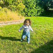 Klay joined the competition — help win amazing prizes! child, toddler, grass, outdoor, sunlight, greenery, overalls, curly_hair, walking, lawn, brick_wall, hedge, casual_clothing, daylight, nature, smiling, playful, person, young_child, park