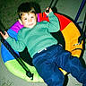 child, boy, swing, playground, colorful, green_sweater, blue_pants, white_shoes, grass, night, outdoor, play, rope, happy, casual_clothing, leisure, smile, fun, young, relaxed