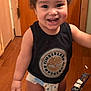 baby, black_shirt, child, clothing, curly_hair, cute, diaper, door, expression, floor, happy, home, indoor, person, smile, standing, timberland_logo, toddler, tooth, wooden_floor