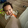 bright, candid, casual, child, clothing, container, curly_hair, floor, happy, holding, indoor, living_room, person, playful, shoe, smiling, toddler, toy, wooden_floor, young_child