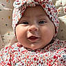 baby, infant, face, headband, smile, blue_eyes, floral_pattern, clothing, cute, child, portrait, closeup, soft_lighting, indoors, bed, blanket, fabric, person, headwear, happy