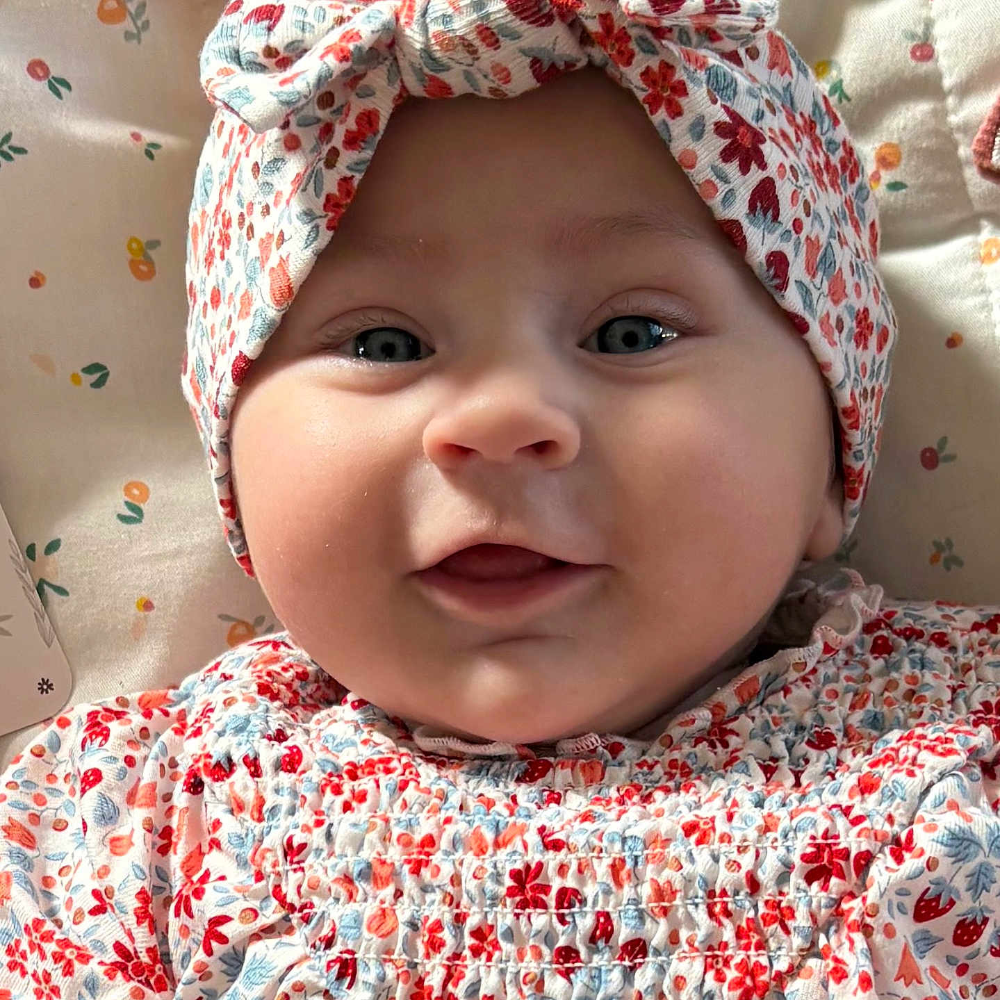 Jade a rejoint le concours — aidez-le/la à gagner de superbes lots ! baby, infant, face, headband, smile, blue_eyes, floral_pattern, clothing, cute, child, portrait, closeup, soft_lighting, indoors, bed, blanket, fabric, person, headwear, happy