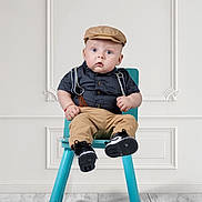 Victor is registered to the contest to win money with this photo: baby, child, blue_eyes, suspenders, khaki_pants, cap, chair, footwear, black_shoes, indoor, wood_floor, white_wall, expression, portrait, sitting, fashion, cute, young_child, person, studio