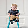 baby, child, blue_eyes, suspenders, khaki_pants, cap, chair, footwear, black_shoes, indoor, wood_floor, white_wall, expression, portrait, sitting, fashion, cute, young_child, person, studio