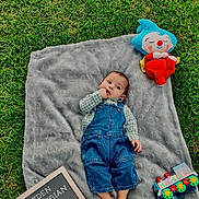Jayden is registered to the contest to win money with this photo: baby, child, infant, outdoor, grass, blanket, denim_overalls, plaid_shirt, plush_toy, clown_doll, colorful_toy, letter_board, portrait, lying_down, looking_at_camera, hand_to_mouth, monthly_milestone, natural_light, greenery, family_photo