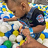 toddler, child, ball_pit, colorful_balls, overalls, paw_patrol, holding_hand, earring, indoor_play_area, black_shirt, wristband, curly_hair, netting, playground, person, young_child, fun, exploring, close_up, hand
