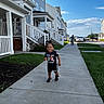 toddler, child, sidewalk, suburban, daytime, grass, house, porch, stairs, bike, boy, sky, clouds, casual_clothing, shoes, smile, outdoor, residential_area, happy, person