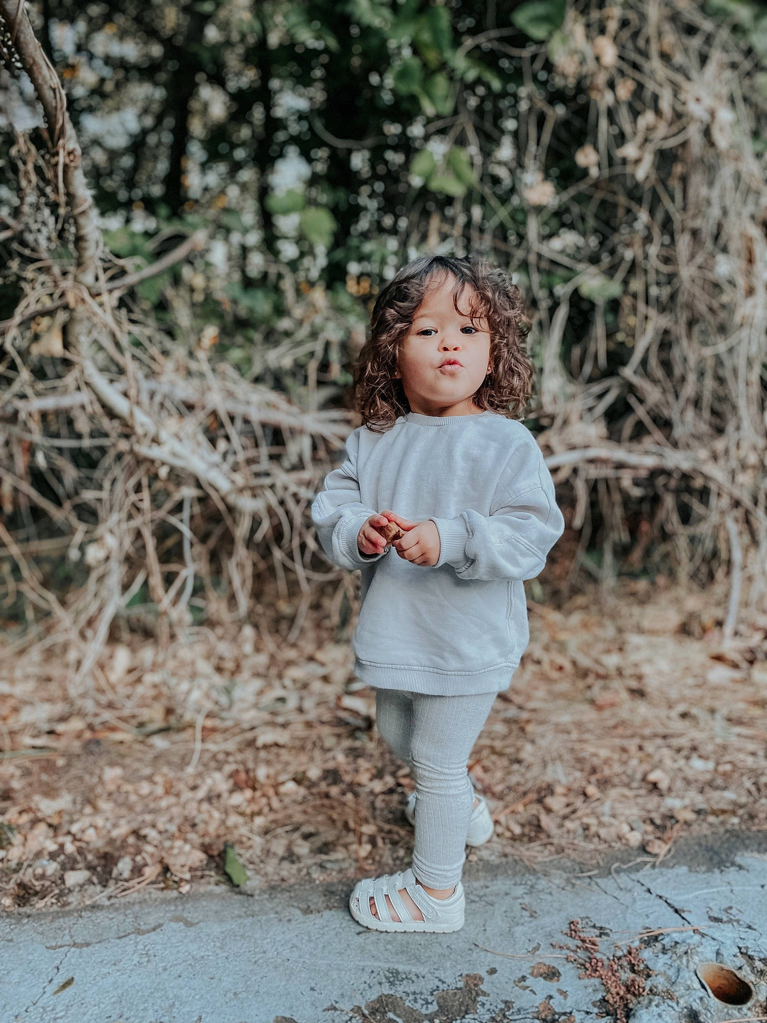 Ella Grace is registered to the contest to win money with this photo: blond, brown_hair, doll, fawn, forest, fur, grass, happy, people_in_nature, person, plant, recreation, sitting, toddler, toy, tree, trunk, twig, winter, wood
