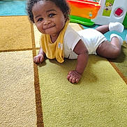 Elijah joined the competition — help win amazing prizes! baby, child, indoor, carpet, smile, yellow_bib, white_socks, curly_hair, play_area, toy, floor, cute, happy, person, infant, toddler, home, crawling, colorful, playtime