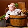 baby, infant, headband, wooden_bucket, bench, greenery, fur_pillow, white_outfit, portrait, studio, smile, chubby_cheeks, wooden_floor, prop, hand, eyes, cute, rustic, brown_background, basket