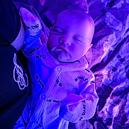 Charlie is registered to the contest to win money with this photo: baby, sleeping, onesie, purple_light, blanket, floral_pattern, infant, clothing, bed, rest, peaceful, person, soft_lighting, cute, portrait, newborn, fabric, hand, closeup, indoor