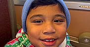 George is registered to the contest to win money with this photo: child, smiling, portrait, beanie, winter_clothing, christmas, festive, train, train_interior, window, seated, face, eyes, teeth, jacket, colorful, cozy, indoors, travel, happy