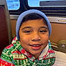 child, smiling, portrait, beanie, winter_clothing, christmas, festive, train, train_interior, window, seated, face, eyes, teeth, jacket, colorful, cozy, indoors, travel, happy